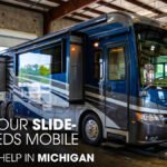 An RV parked inside a workshop garage undergoing a slide-out repair job
