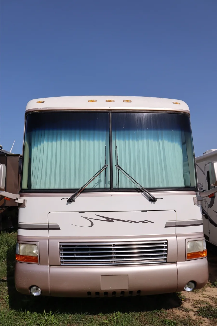 Cream-and-rose Class A motorhome photographed straight-on from the front at the Nagel Trailer Repair yard in Merrill, Michigan