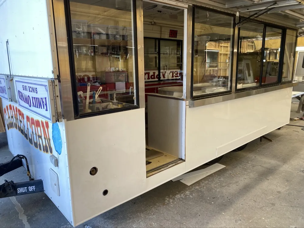 The same concession trailer finished — clean white panels, glass serving windows, lettering on