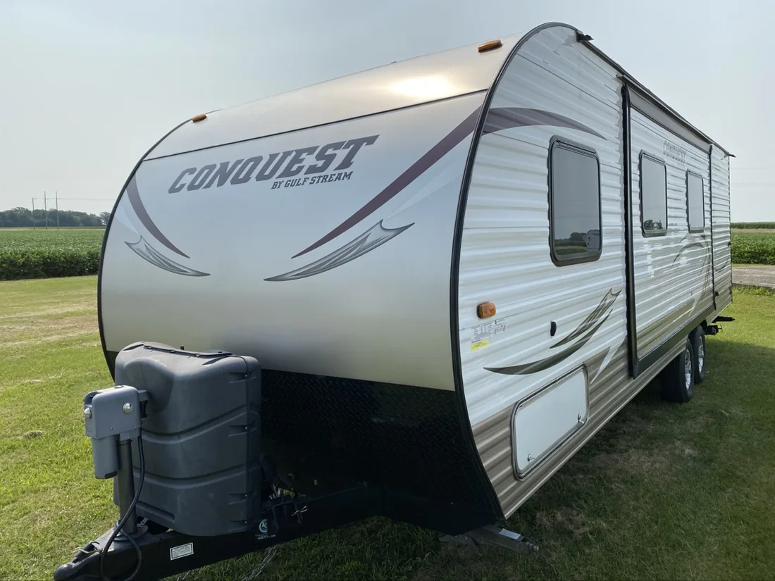 Gulf Stream Conquest travel trailer, front three-quarter on grass — white and champagne corrugated body with maroon sweep graphics and black trim