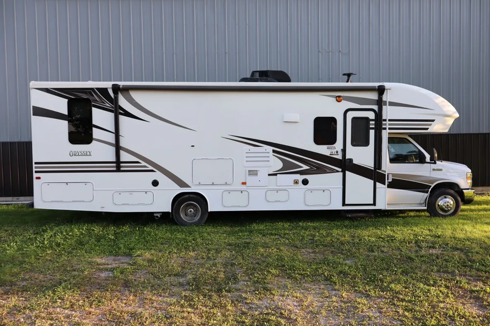 White Entegra Odyssey Class C motorhome in side profile on the grass in front of the shop barn at Nagel Trailer Repair