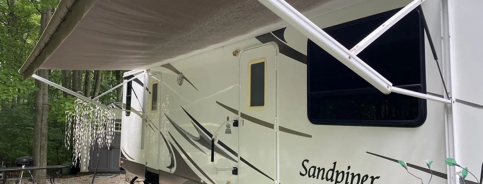 Sandpiper fifth wheel with its patio awning out and slide extended at a wooded Michigan campsite — the kind of rig Nagel Trailer Repair keeps road-ready in Merrill, Michigan