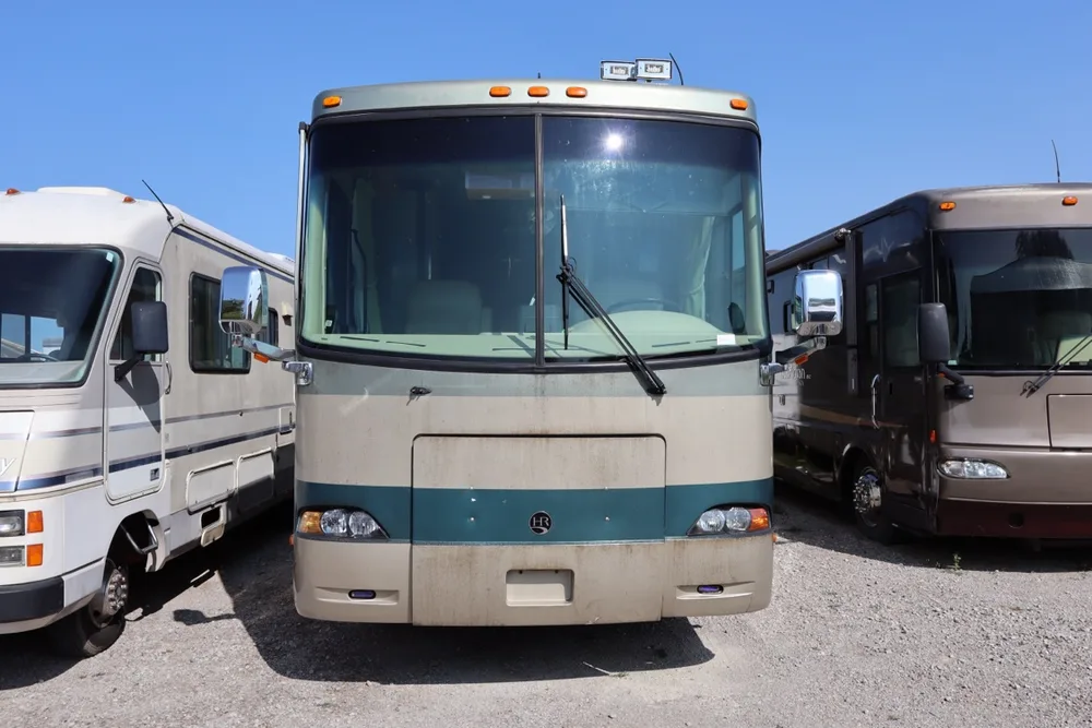 Beige and teal Holiday Rambler motorhome photographed straight-on, flanked by two other motorhomes at the shop yard in Merrill, Michigan