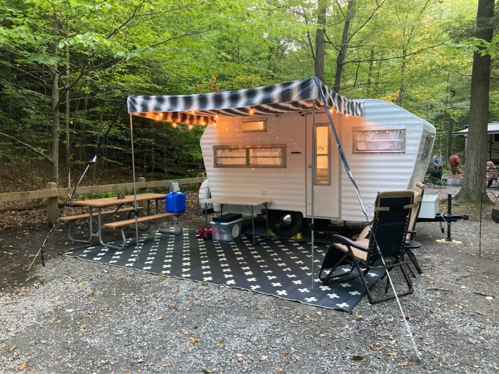 Stage 5 of the rebuild — the finished camper set up at a wooded campsite under a checkered awning