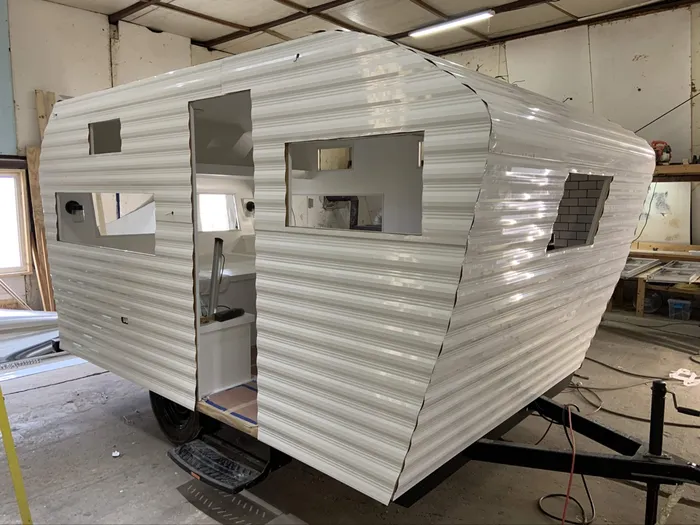 Stage 3 of the rebuild — fresh white corrugated aluminum siding on the camper, window openings cut