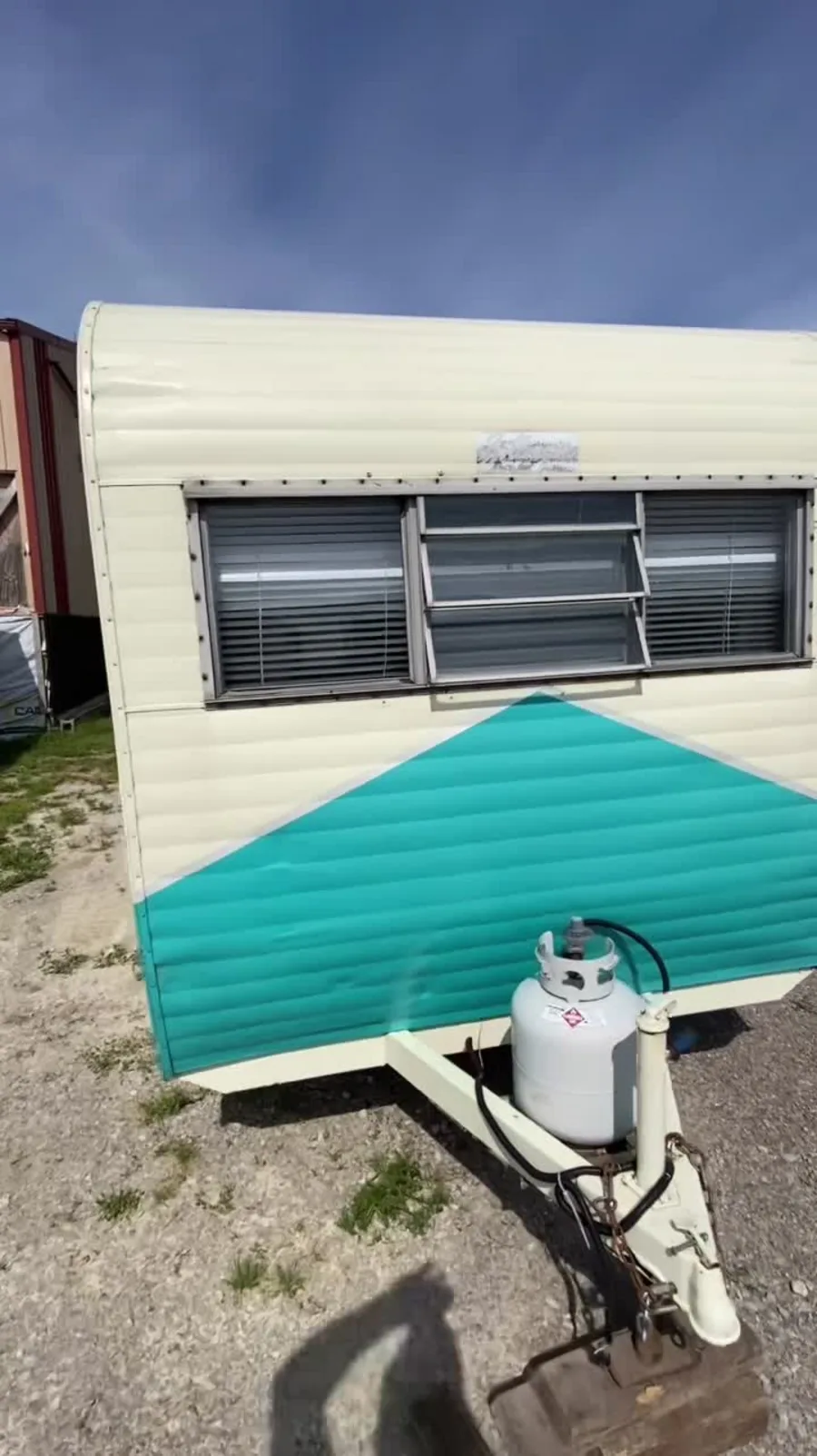 The same restored vintage camper straight-on from the front — turquoise chevron, propane tank, fresh paint