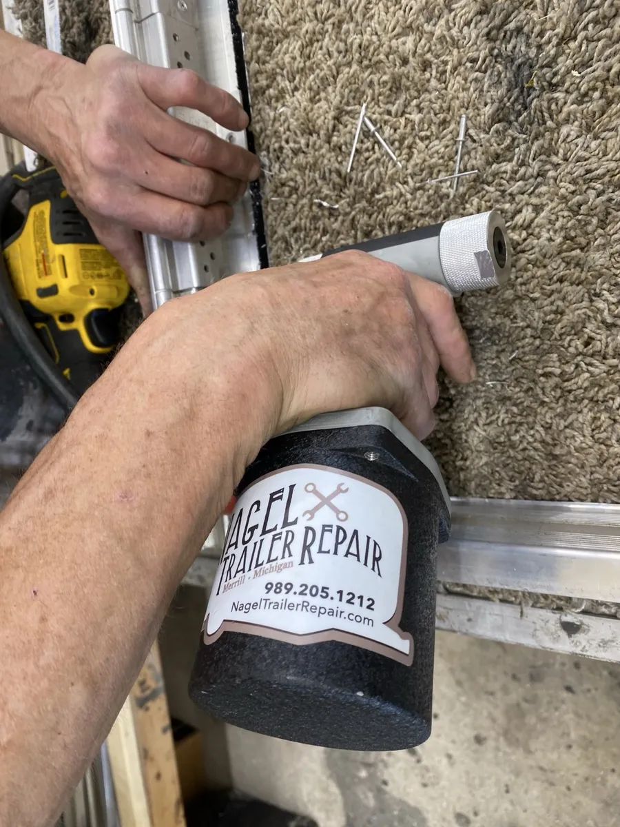 Hands driving rivets with a pneumatic rivet gun carrying the shop’s own Nagel Trailer Repair sticker — craftsmanship detail at the Merrill, Michigan shop