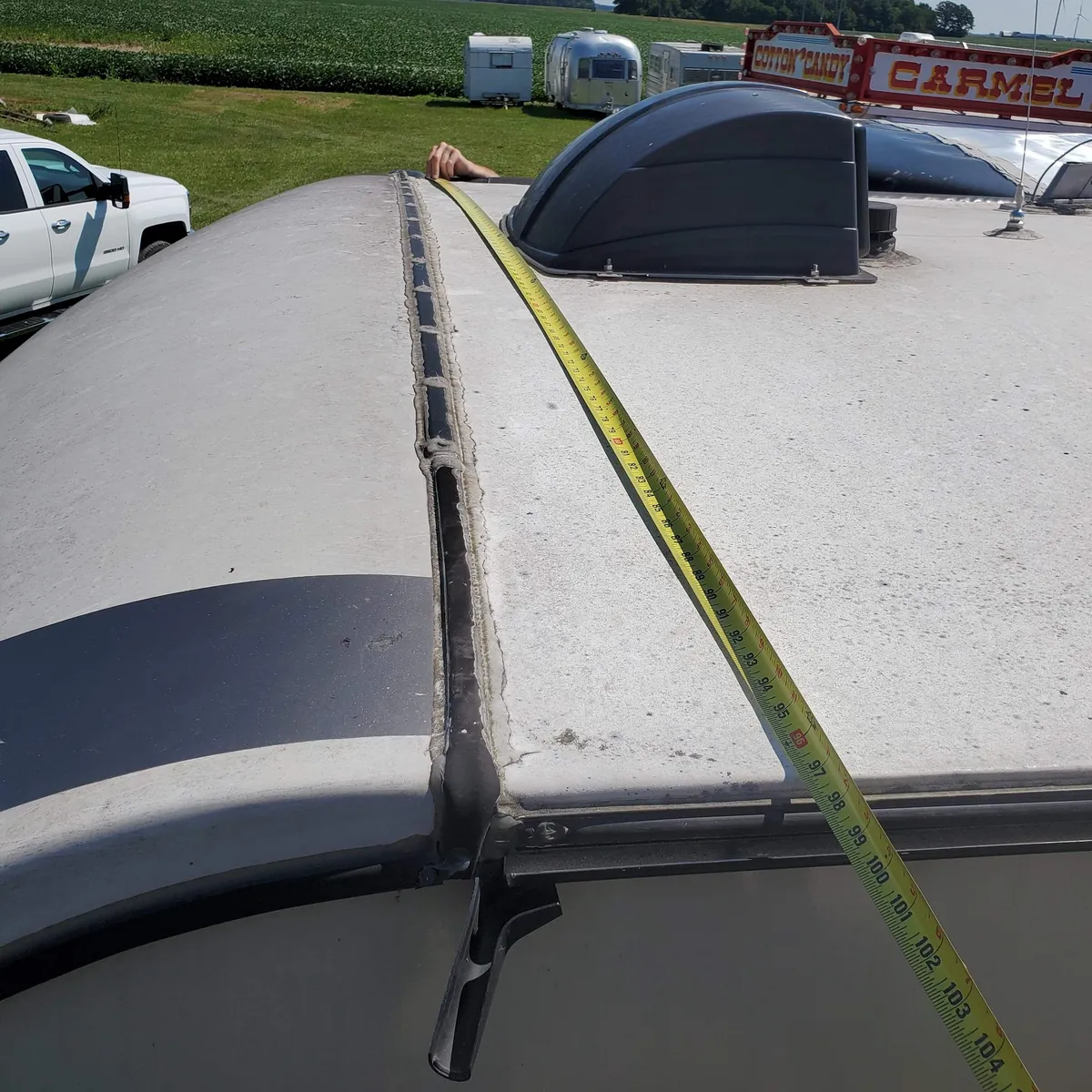 Measuring a roof seam during an RV roof repair at Nagel Trailer Repair in Merrill, Michigan, vintage campers and a concession trailer in the yard behind