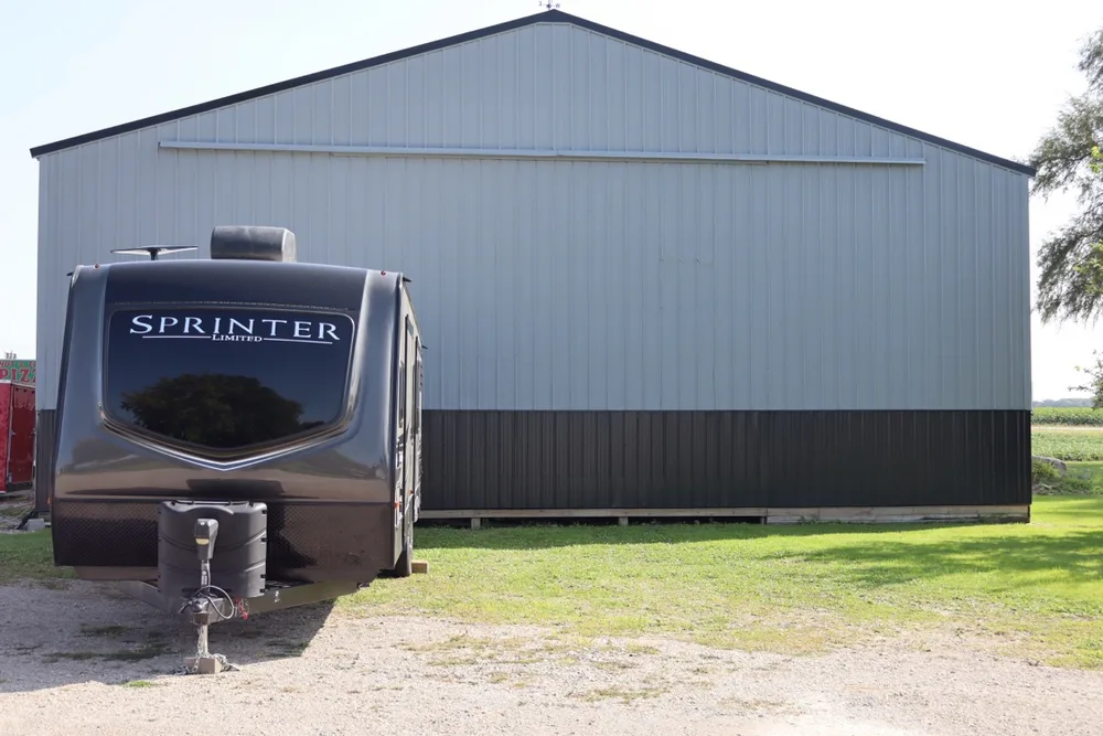 Dark Keystone Sprinter Limited travel trailer parked in front of the gray shop barn at Nagel Trailer Repair in Merrill, Michigan