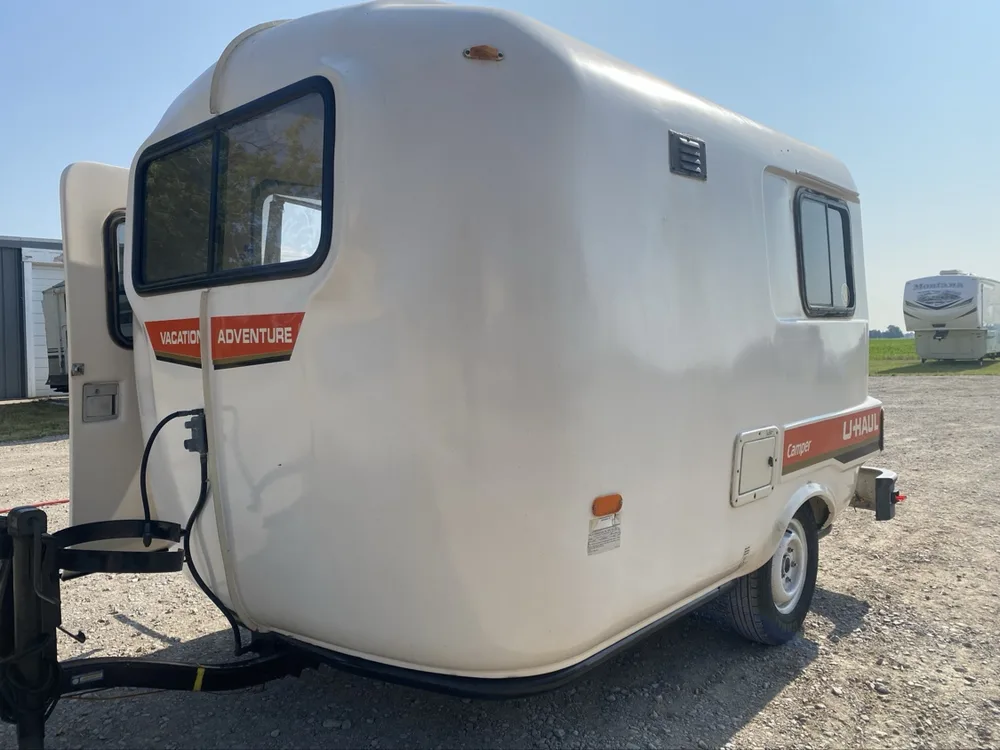 Vintage U-Haul fiberglass egg camper, front three-quarter view with the hitch down, at the yard at Nagel Trailer Repair in Merrill, Michigan