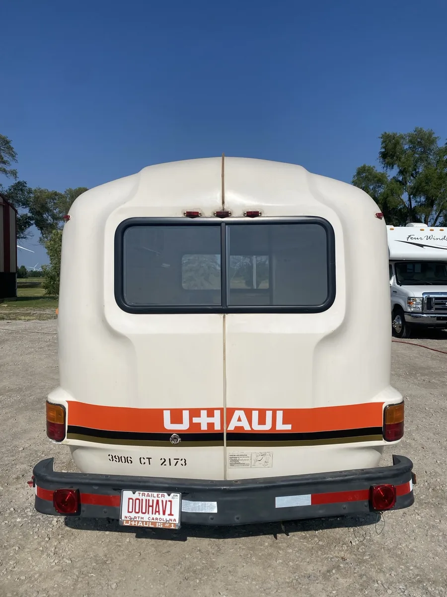 The same vintage U-Haul fiberglass egg camper straight-on from the rear — orange U-Haul stripe across the back