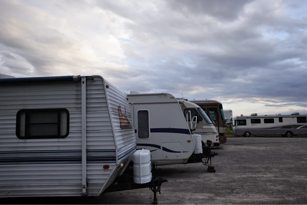 Travel trailers and motorhomes in a row at the Nagel Trailer Repair yard under a dramatic cloudy dusk sky