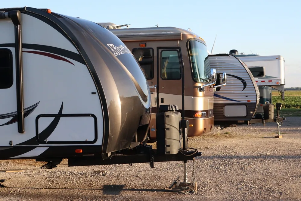 Yard row in warm golden light at Nagel Trailer Repair — North Trail nose, rose Class A, and more trailers behind